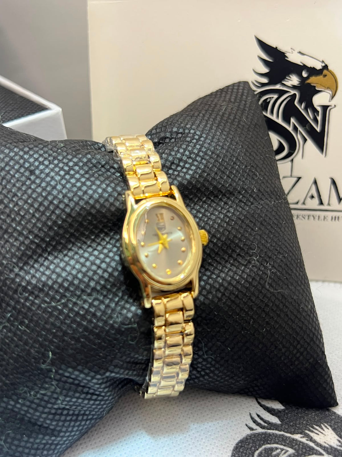 True Worth Ladies Gold-Tone Oval Watch showing champagne dial with gold dot markers and rectangular-link gold bracelet on black pillow
