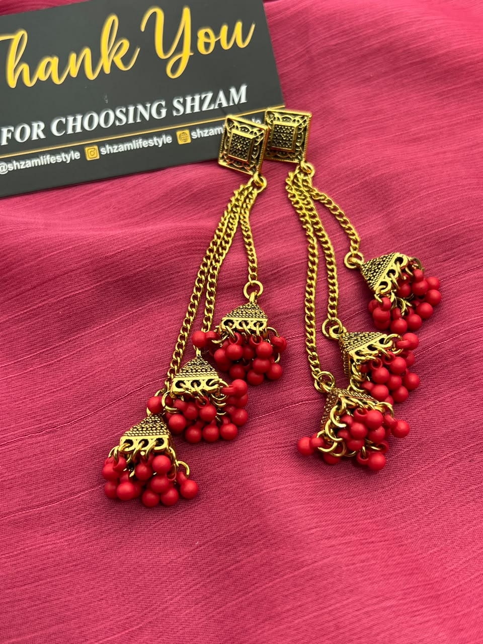 Red Antique Gold Tiered Jhumka Chandelier Earrings on pink fabric