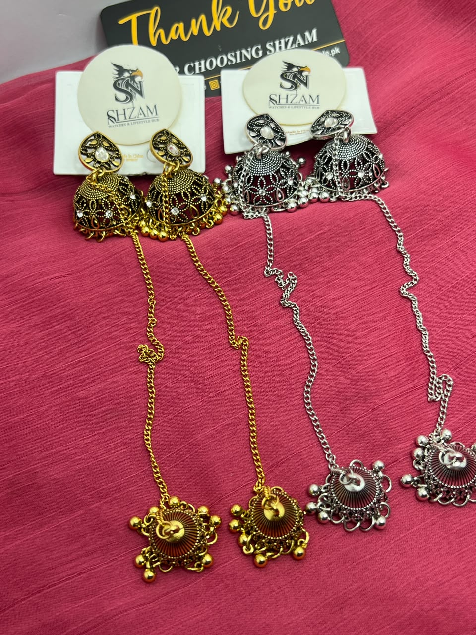 Antique Gold and Oxidized Silver Jhumka Earrings with Chain and Tikka both pairs on pink fabric with Shzam cards